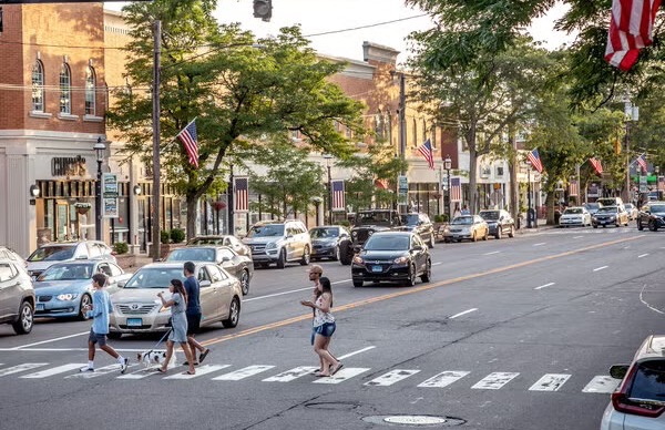Storefronts line a road where pedestrians are crossing